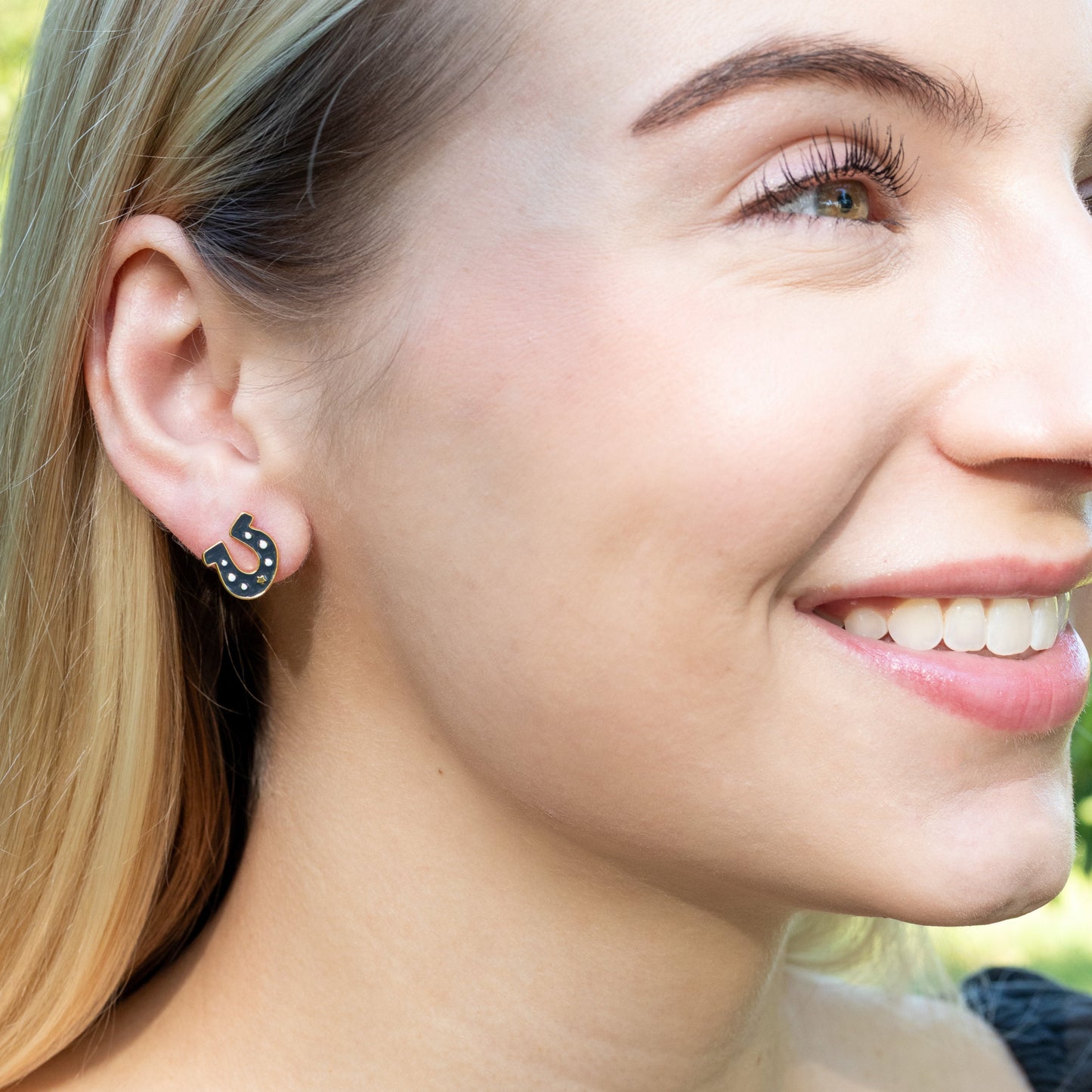 Close-up of a woman's face wearing dark gray horseshoe earring with a blurred natural background