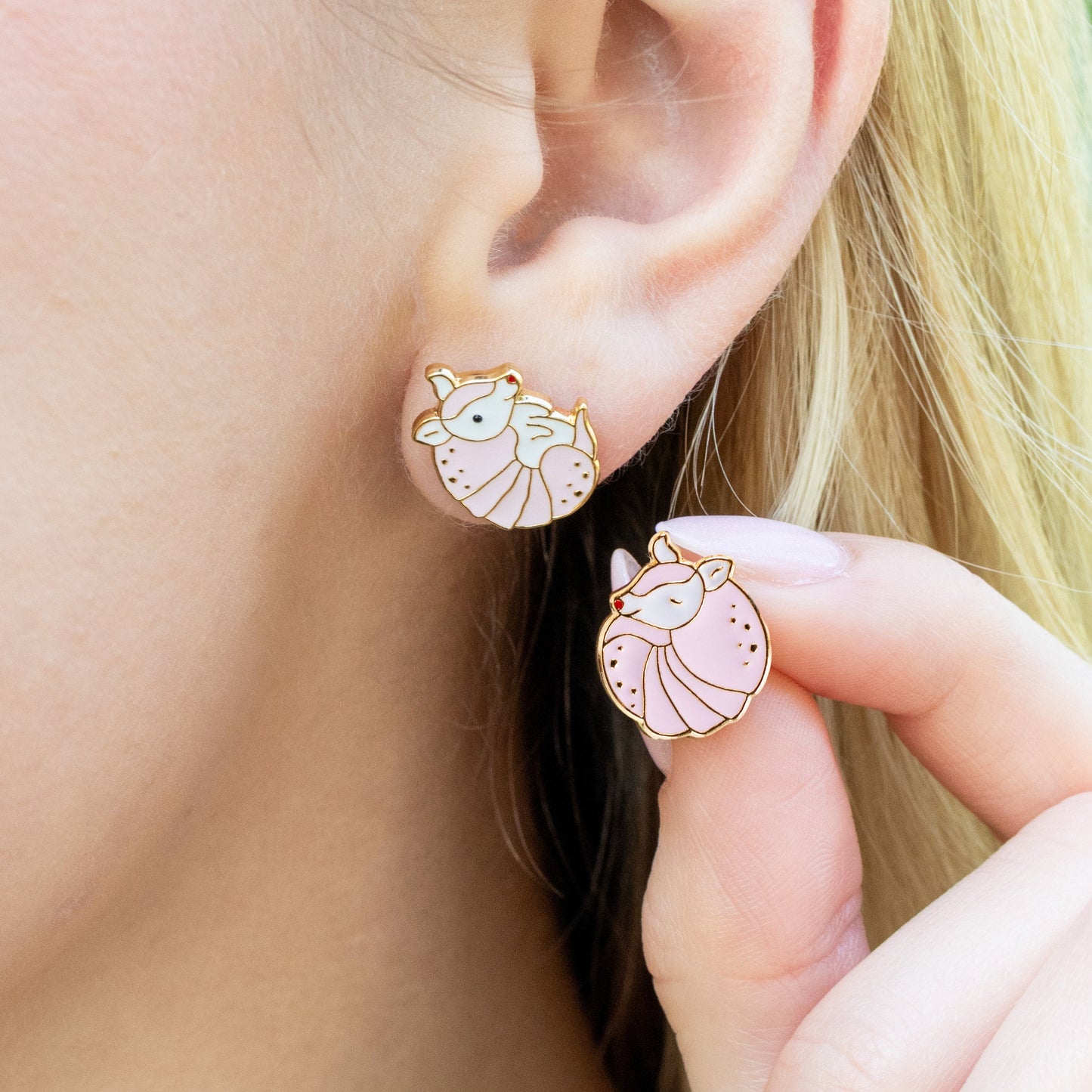 Close-up of a person wearing a pink armadillo shaped stud earrings.