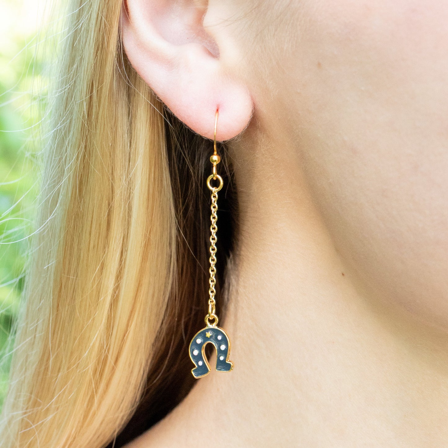 Long Chain Earring with horseshoe charm facing down worn by a person with blonde hair.
