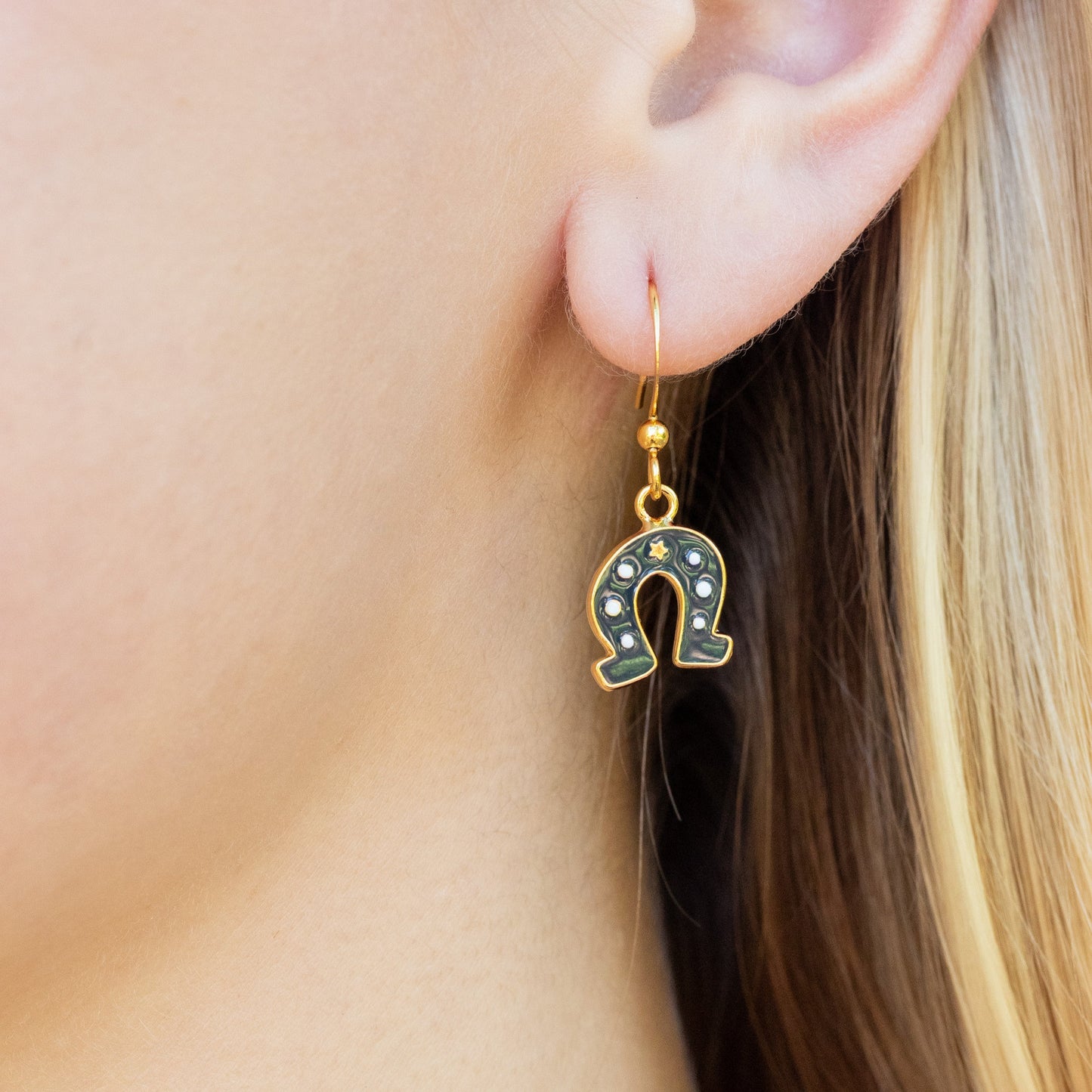 Horseshoe-shaped drop earring worn by a person with blonde hair.