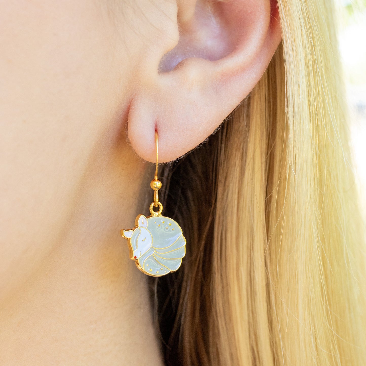 Close-up of a person wearing an tan armadillo drop earring.