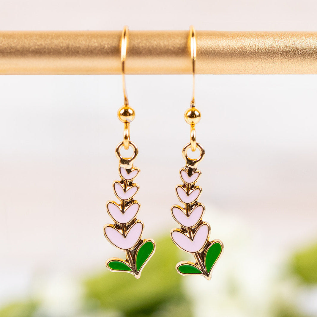 Drop earrings with Texas Pinkbonnet designs on a gold rod against a blurred natural background.