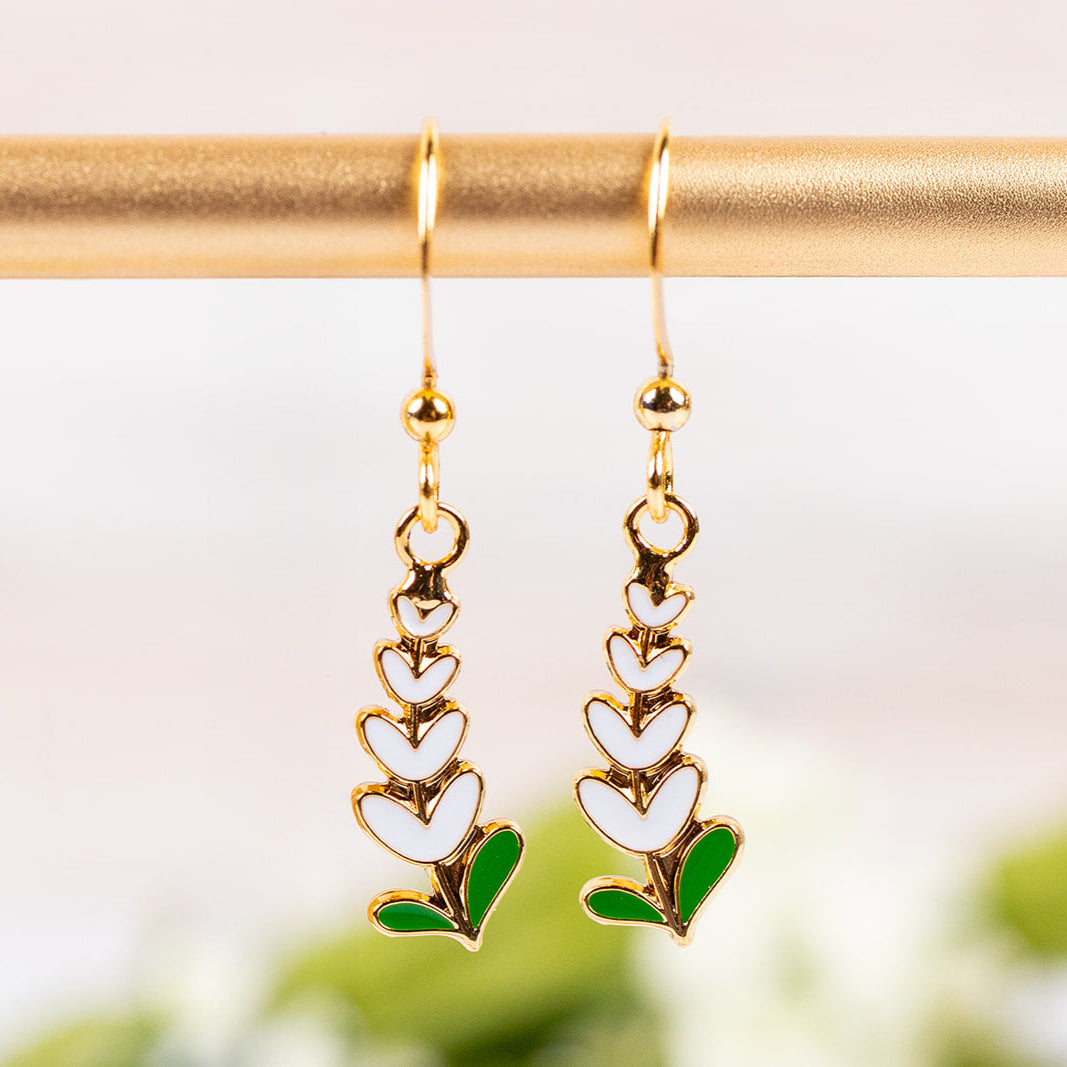Drop earrings with Texas Whitebonnet designs on a gold rod against a blurred natural background.