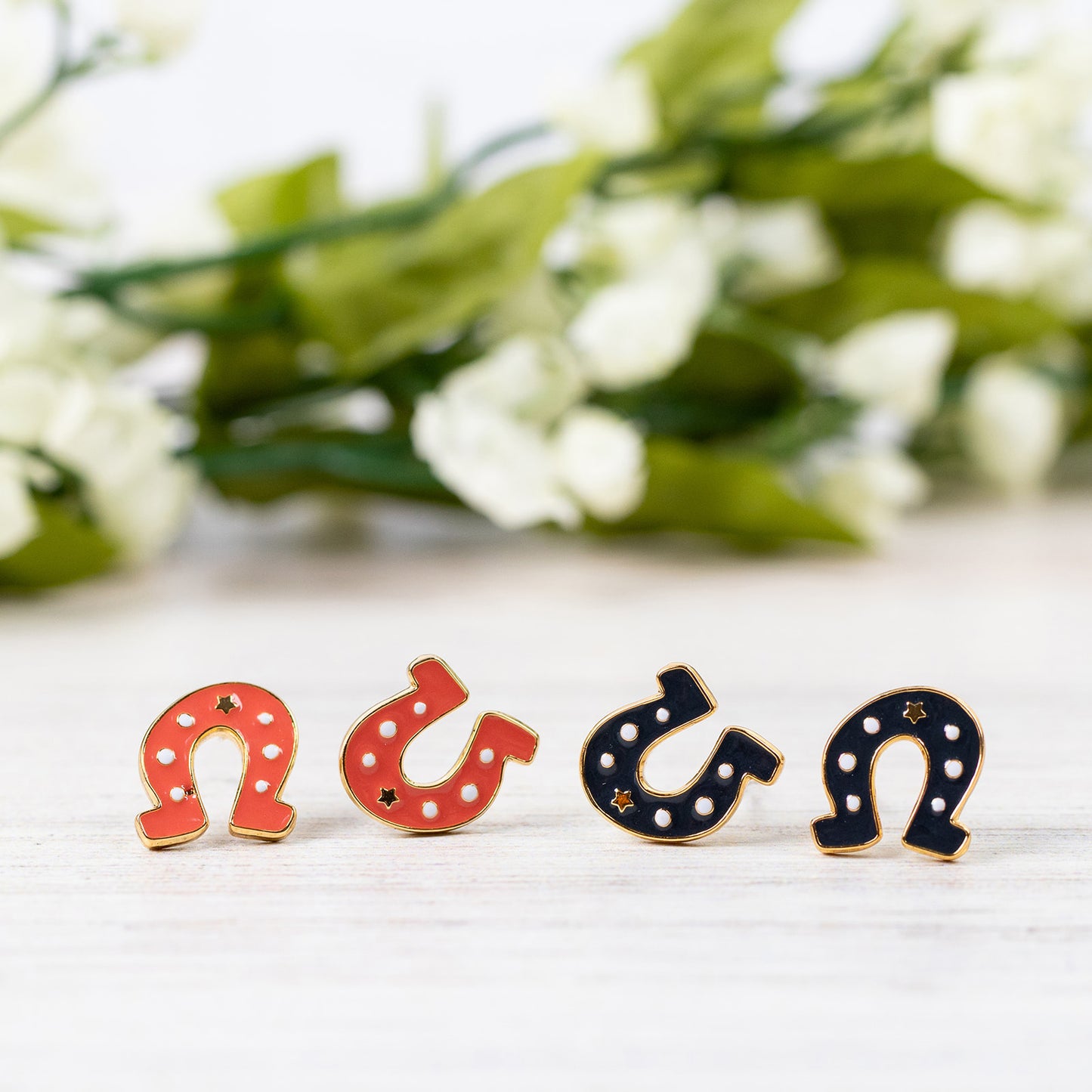 Four dark gray and red orange horseshoe studs on a white surface with blurred greenery in the background.