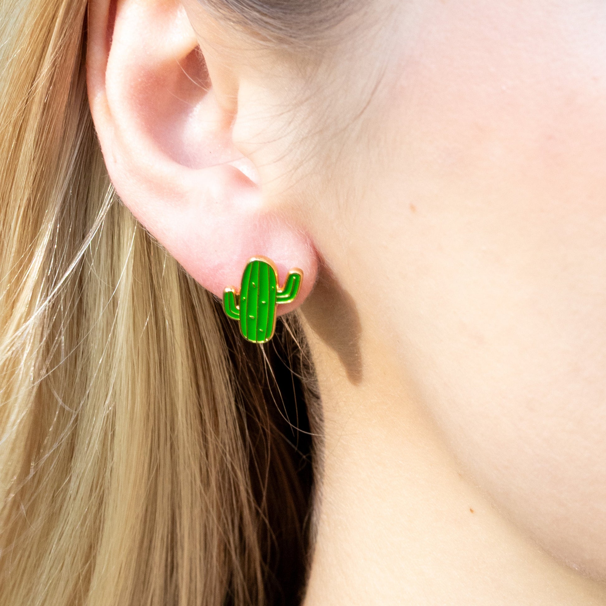 Green cactus-shaped earrings worn by a person with blonde hair.