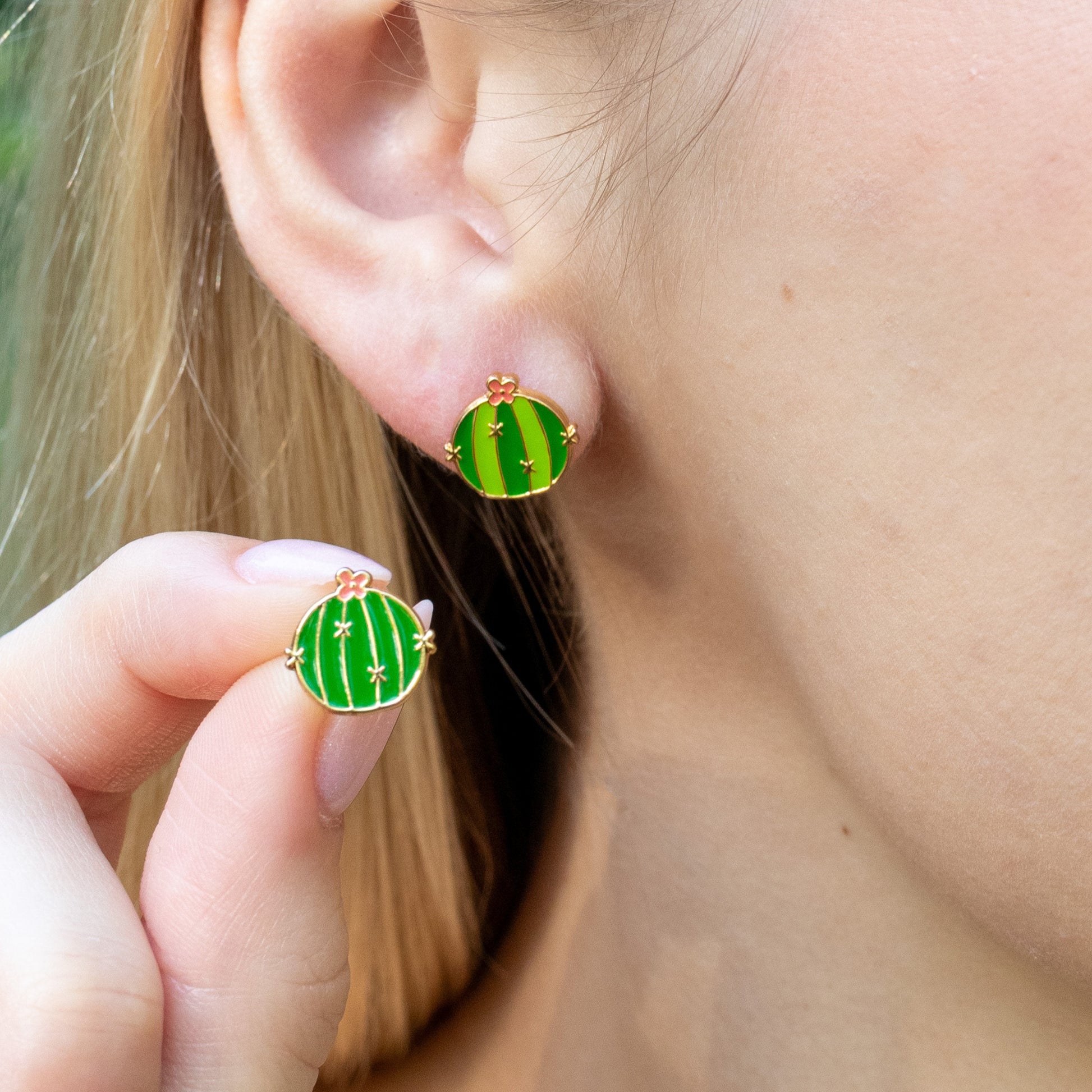 Close-up of a person wearing barrel cactus earrings with a blurred background.