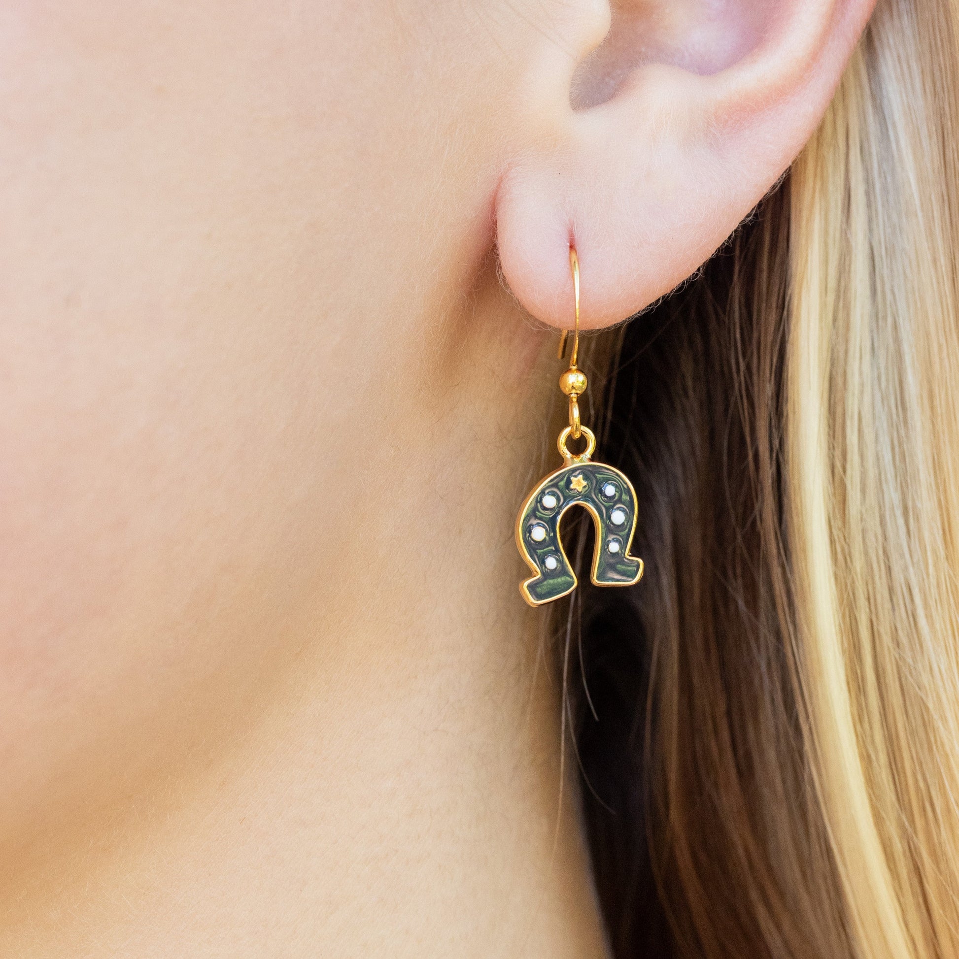 Horseshoe-shaped drop earring worn by a person with blonde hair.