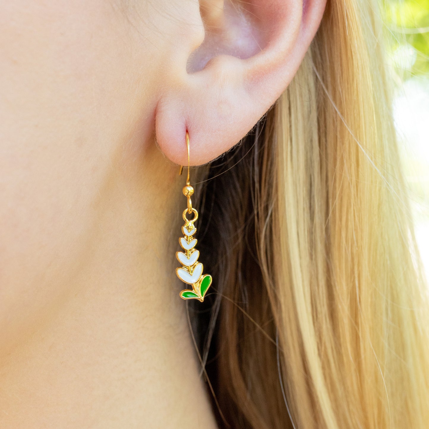 Close-up of an ear wearing a drop earring with Texas White-bonnet flower, blurred background