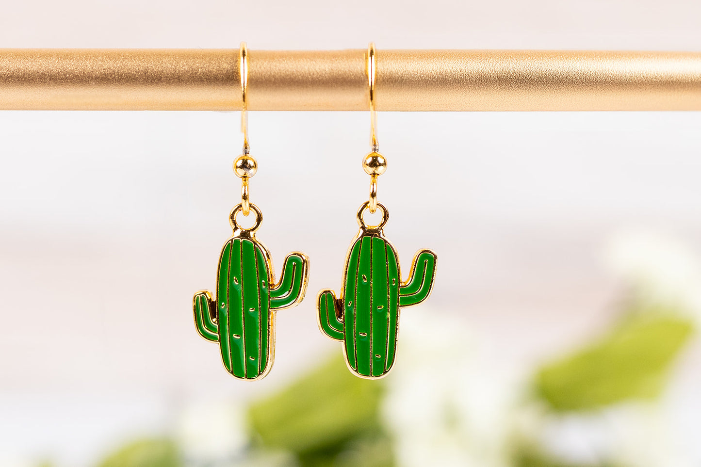 Green cactus-shaped earrings on gold hooks against a blurred green background