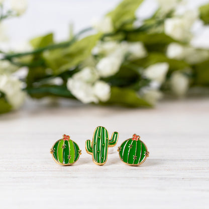 Cactus-shaped earrings on a light surface with a blurred floral background
